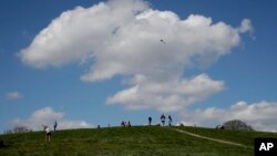 Personas en Primrose Hill, en Londres, disfrutan el día mientras alguien vuela una cometa. Los parques en la ciudad siguen abiertos con una advertencia de cierre si no se respeta el distanciamiento social. Sábado 4 de abril de 2020. 