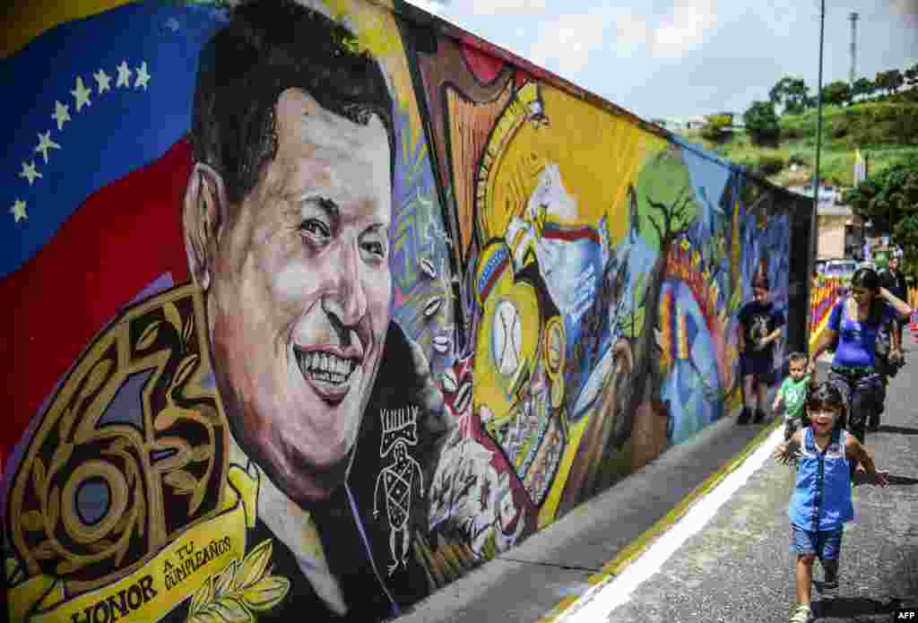 ក្មេងៗ​ដើរ​កាត់គំនូរ​អតីត​ប្រធានាធិបតី​ប្រទេស​វ៉េណេស៊ុយអេឡា​ Hugo Chavez នៅក្នុង​ទីក្រុង​ការ៉ាកាស​ក្បែរសារមន្ទីរ​ &laquo;Cuartel de la Montaña&raquo; ទី​តម្កល់សព​ក្នុង​ខួប​កំណើត​ទី​៦៣ របស់លោក។