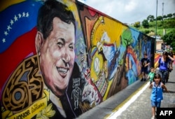 FILE: Children walk by a mural depicting late Venezuelan president Hugo Chavez at "23 de Enero" neighborhood in Caracas near the "Cuartel de la Montaña" museum where his body rests, July 28, 2017, on the 63rd anniversary of his birth.