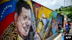 Des enfants marchent devant un mur peint au visage du président Hugo Chavez du Venezuela, 28 juillet 2017.