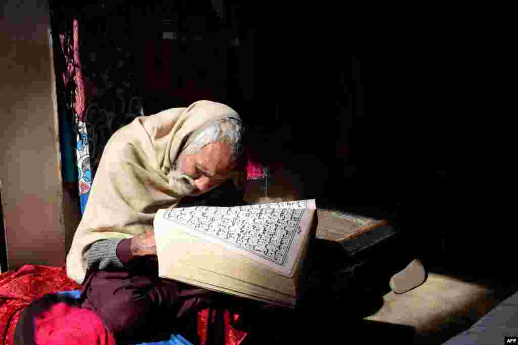Seorang pria lansia penjual pakaian membaca Alquran sambil menunggu pelanggan di tokonya di Lahore, Pakistan.
