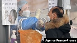 A medical staff member (L-in booth) takes a nasal swab from a visitor as part of a test for the Covid-19 coronavirus at a virus testing center in Seoul on Jan. 26, 2022.