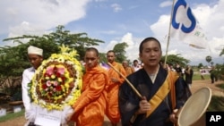 A Buddhist monk from Japan, front right, chants together with a Cambodian Buddhist monk, center, and a Cambodian Muslim, left, as they carry a wreath of flowers to lead a march at Choeung Ek, a former Khmer Rouge killing field, some 16 kilometers (10 mile