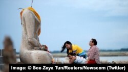 یک خانواده در حال نیایش در مقابل مجسمه بی سر بودا در معبد گمشده ای که در اثر خشکسالی از زیر آب بیرون آمده است. اوت ۲۰۱۹