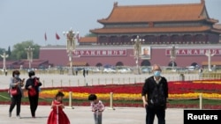 戴着口罩的北京市民在天安门广场为五一劳动节建起的花坛旁散步。（2020年4月29日）