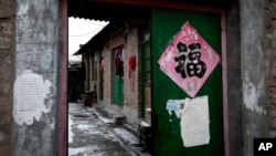 Baju terlihat digantungkan di sebuah pintu masuk berwarna hijau di sebuah rumah batu bata, 5 Februari 2013. (AP Photo/Andy Wong). Rumah ini di kalangan pemerintah Beijing dikenal sebagai "penjara hitam", yang dilaporkan sering dipergunakan oleh pejabat lokal untuk memenjarakan warga setempat secara ilegal.