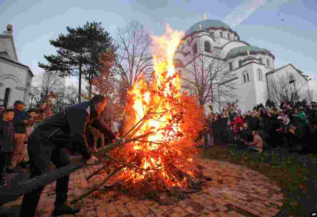 A man pushes oak tree branches into a fire burning outside the St. Sava church, on Orthodox Christian Christmas Eve in Belgrade, Serbia, Jan. 6, 2018.