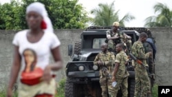 A woman walks past soldiers loyal to Alassane Ouattara as they man a checkpoint at one of the principal entrances to Abidjan, Ivory Coast, April 5, 2011