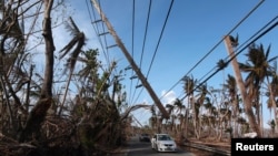 Cars drive under a partially collapsed utility pole, after the island was hit by Hurricane Maria in September, in Naguabo, Puerto Rico Oct. 20, 2017.