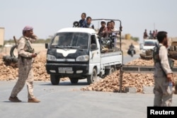 Syria Democratic Forces (SDF) fighters man a checkpoint as civilians on pick-up trucks evacuate from the southern districts of Manbij city after the SDF advanced into it in Aleppo Governorate, Syria, July 1, 2016.
