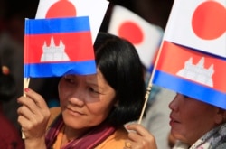 FILE - Cambodians hold Japan's flags and their national flags as they listen to Prime Minister Hun Sen's speech during an inauguration ceremony of a road funded by Japan for its official use at Kdey Takoy village, outside of Phnom Penh, Cambodia, Tuesday, March 13, 2018. (AP Photo/Heng Sinith)