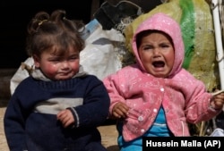 In this Tuesday, Feb. 19, 2013 photo, two Syrian refugee children sit outside their family tent, at Atmeh refugee camp, in the northern Syrian province of Idlib, Syria. This rebel-controlled camp only yards from the border with Turkey houses some 16,000 p