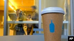 In this Thursday, Dec. 12, 2019 photo, a Blue Bottle Coffee paper to-go cup rests on a table outside one of their cafes in San Francisco. The Oakland-based chain says it's getting rid of disposable cups at two locations next year.