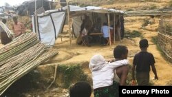 Rohingya refugees walk along a litter-strewn path next to makeshift tents at a camp in Bangladesh.