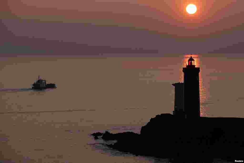 A boat makes his way behind the Phare du Petit Minou as the sun sets over the Atlantic Ocean on a cold winter day in Plouzane, France.