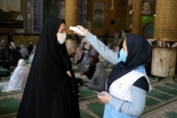 FILE - A woman wearing a protective face mask checks the temperature of a worshipper, also with mask, ahead of Friday prayers at Qarchak Jamee Mosque, in Qarchak, Iran, June 12, 2020. (WANA/Ali Khara via Reuters)