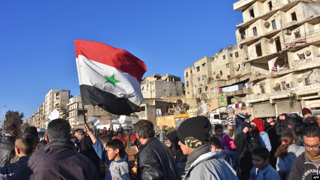 A young boy waves the Syrian flag as residents in a government-held area of Aleppo gather in the street during an evacuation operation of rebel fighters and their families from rebel-held neighborhoods in Syria's northern embattled city on Dec. 15, 2016.