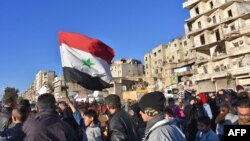 A young boy waves the Syrian flag as residents in a government-held area of Aleppo gather in the street during an evacuation operation of rebel fighters and their families from rebel-held neighborhoods in Syria's northern embattled city on Dec. 15, 2016.