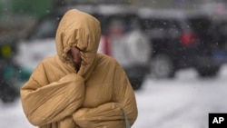 Seorang perempuan menggunakan pakaian musim dinginnya untuk melindungi badannya dari angin dan salju yang muncul di jalanan kota Beijing saat ibu kota China itu dilanda oleh badai salju pada 7 November 2021. (Foto: AP/Andy Wong)