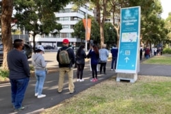 FILE - People wait in line outside a coronavirus disease (COVID-19) vaccination center at Sydney Olympic Park in Sydney, Australia, June 23, 2021.