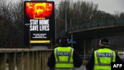 Police officers walk past a COVID-19 information board alongside the Clydeside Expressway in Glasgow, Jan. 20, 2021. 
