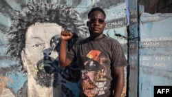 Higino Fumo, 32 anos, conhecido no mundo do rap como “Nikotina” levanta o punho enquanto posa para um retrato junto a um mural em memória do rapper Mano Azagaia e crítico da Frelimo, que morreu em 2023, em Maputo, a 3 de dezembro de 2024.