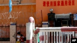新疆喀什地區伽師縣一所小學校門有鐵絲網和監控鏡頭，校門前寫著：請使用國家通用語言。（2018年8月31日）