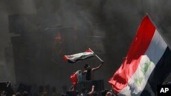 Anti-government protesters burn tires in front of barriers set up by security forces to close the Jumhuriyah Bridge leading to the Green Zone government area, during ongoing protests in Baghdad, Iraq, Sunday, May 10, 2020.