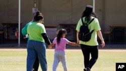 A child holds hands with workers at an emergency shelter for migrant children July 2, 2021, in Pomona, Calif. 
