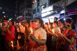 Women wearing red ribbons hold candles during a night protest against the military coup in Yangon, Myanmar, Feb. 5, 2021.