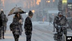 FILE - Two pedestrians wait for a bicycle to pass before crossing a snow-covered shopping street in Amsterdam, Netherlands, Monday, Dec. 11, 2017.