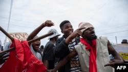 Manifestantes seguram uma cruz com a bandeira do partido Frente de Libertação de Moçambique (FRELIMO) enquanto protestam no bairro de Hulene, em Maputo, a 31 de outubro de 2024, durante o primeiro dia da greve nacional convocada pela oposição moçambicana.