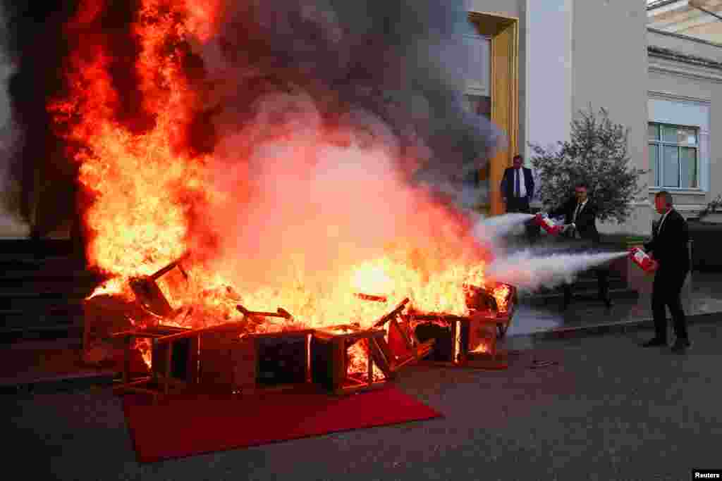 National Guard extinguishes a fire as members of the opposition burn their chairs outside the parliament building to protest against the government and the imprisonment of their colleague Ervin Salianji, in Tirana, Albania.