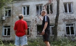 FILE - Men speak outside a residential building, which locals said was damaged during recent shelling, in the suburb of the rebel-controlled city of Donetsk, Ukraine, June 28, 2019.
