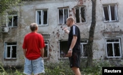FILE - Men speak outside a residential building, which locals said was damaged during recent shelling, in the suburb of the rebel-controlled city of Donetsk, Ukraine, June 28, 2019.
