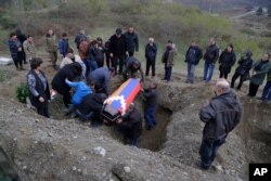 FILE - Relatives and friends of Mkhitar Beglarian, an ethnic Armenian soldier of the Nagorno-Karabakh army, killed during fighting in the enclave, lower his coffin into a grave during his funeral in Stepanakert, Nov. 15, 2020.