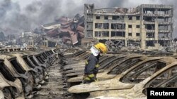 A firefighter walks among damaged vehicles as smoke rises amid shipping containers at the site of explosions, in Tianjin, China, Aug. 14, 2015.