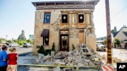 FILE - Pedestrians stop to examine a crumbling building facade in Napa, California, following an earthquake, Aug. 24, 2014. 