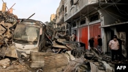 People walk past a bus that is half-buried in rubble as they search for survivors and the bodies of victims through buildings that were destroyed during Israeli bombardment, in Khan Yunis in the southern Gaza Strip on Oct. 25, 2023.