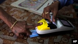 FILE - A woman places her finger on a biometric card reader before buying her quota of subsidized rice from a fair price shop under the Public Distribution System in Rayagada, in the Indian eastern state of Orissa, March 20, 2012.