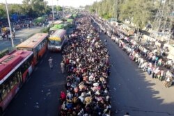 FILE - Migrant workers and their families line up in a New Delhi bus terminal to leave for their villages during a government-imposed nationwide lockdown as a preventive measure against the coronavirus, March 28, 2020.