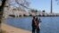 A man and woman pose for a selfie under blooming Yoshino cherry trees on the edge of the Tidal Basin, Tuesday, March 30, 2021, in Washington.