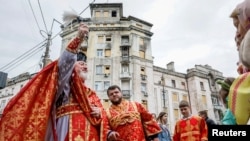 在基輔的聖尼古拉斯教堂外，神職人員在東正教復活節活動中為一棟被俄羅斯飛彈損壞的居民樓揮灑聖水。 (2024年5月5日)