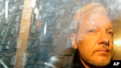 FILE - In this May 1, 2019 file photo, buildings are reflected in the window as WikiLeaks founder Julian Assange is taken from court, where he appeared on charges of jumping British bail seven years ago, in London. 