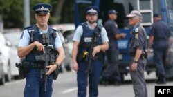 Armed police keep watch as people pay their respects in front of floral tributes for victims of the March 15 mosque attacks, in Christchurch, March 16, 2019.