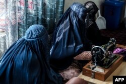 This photograph taken on January 9, 2024 shows Afghan burqa-clad women sewing clothes at a women's community center in Bagrami district on the outskirts of Kabul. (Photo by Wakil KOHSAR / AFP)