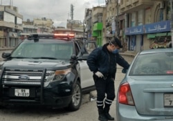 FILE - A policeman speaks to a driver of a car at a checkpoint during a nationawide coronavirus curfew, in the Jordanian capital Amman, March 21, 2020.