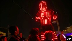 Young participants look at a performer wearing a luminous costume entertaining a crowd in Lisbon, Portugal, during the symbolic switching off of lights known as Earth Hour, March 28, 2015. 