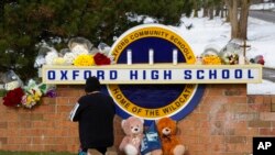 A well wisher kneels to pray at a memorial on the sign of Oxford High School in Oxford, Mich., Dec. 1, 2021.