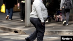 FILE - A man crosses a main road as pedestrians carrying food walk along the footpath in central Sydney, Australia.